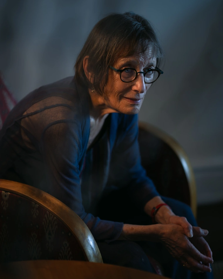 White woman with brown hair and glasses sits in an arm chair.