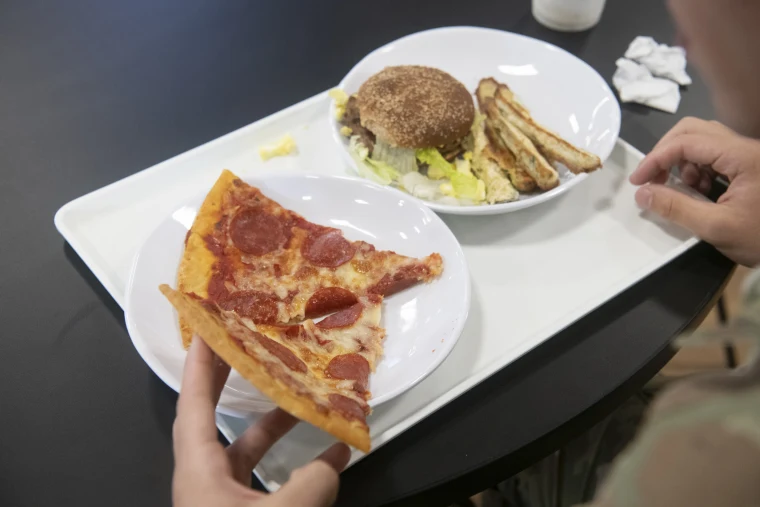 A soldier eats pizza and a burger from Belvedere Bistro on base at Fort Drum, NY, on July 28, 2026.